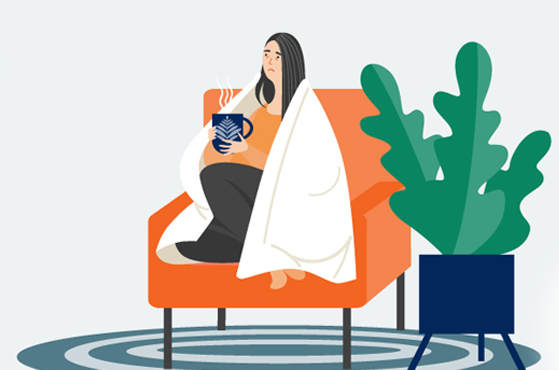 A woman wrapped in a blanket holds a mug of something hot while sitting on a comfortable chair