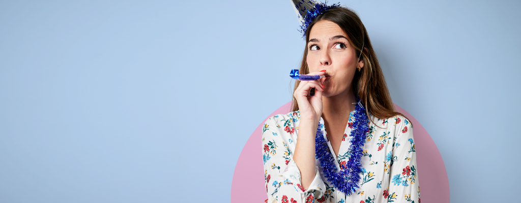 A woman wears a party hat and blows on a noise maker to celebrate