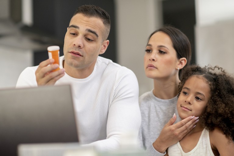 A man looks at a prescription pill bottle while his family watches